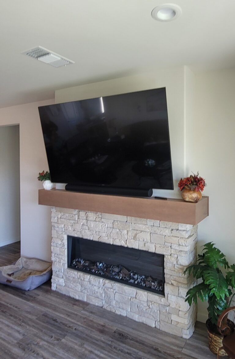 Large TV and sound bar combo mounted together on a tilt wall mount over customer's living room fireplace. TV Mounting Service. Kern County, Bakersfield, CA, USA.